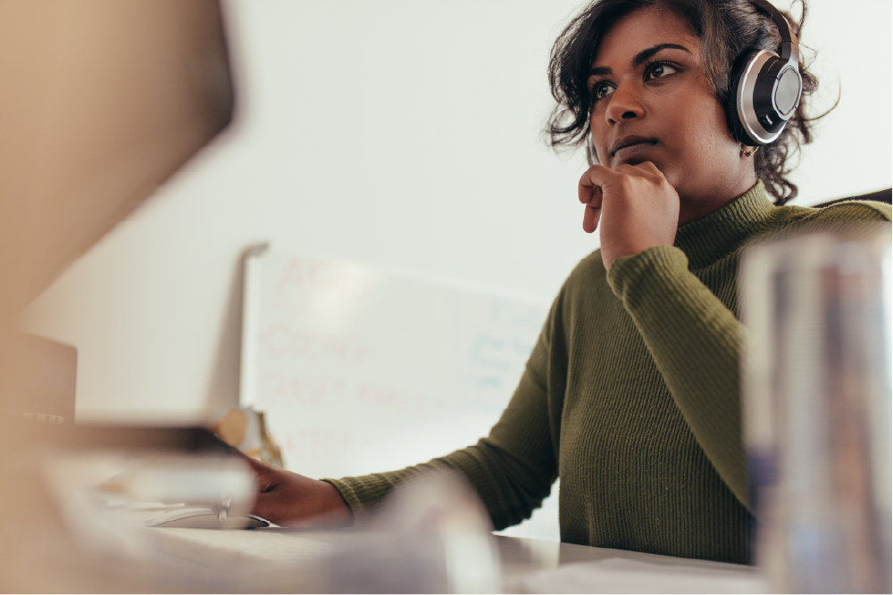 Woman in green sweater focused on computer, surrounded by notes in creative workspace.