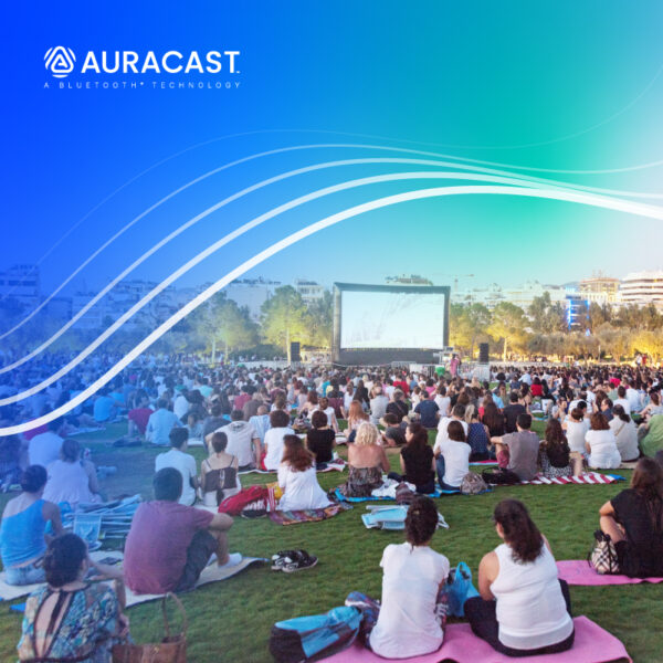 A crowd enjoying an outdoor movie night with Auracast technology in a vibrant park setting.