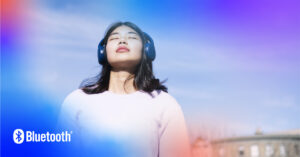 Young woman enjoys music with Bluetooth headphones against a vibrant, swirling blue sky.