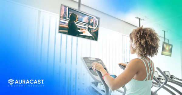 Person using a treadmill in a gym, watching a news program on a screen and listening to the audio through Auracast broadcast audio.
