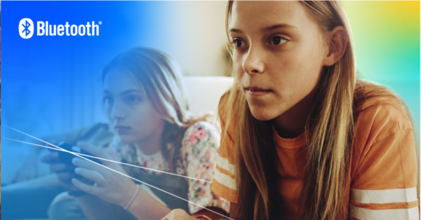 Two girls look forward intently, playing video games with wireless gaming controllers.