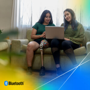 Two people sitting on a couch, looking at a laptop together. One of the individuals has a prosthetic leg.