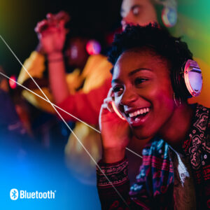 A person with Bluetooth headphones enjoys music at a vibrant colorful event, while another individual dances in the background.